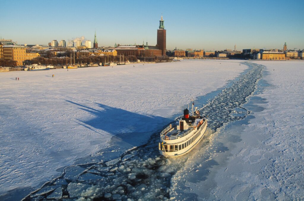 Det snötäckta Stockholms stadshus med en sightseeingbåt som åker över den frusna Riddarfjärden